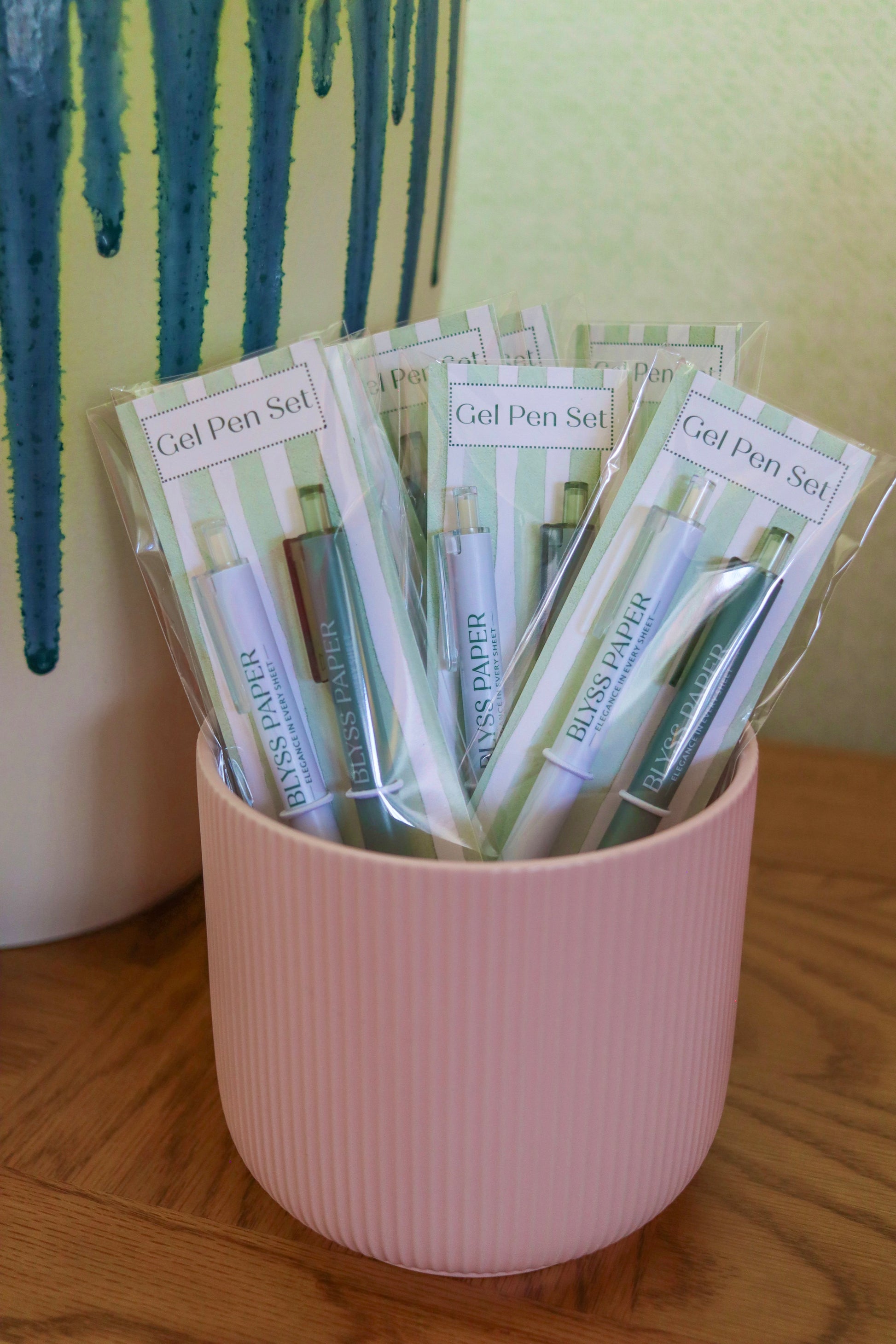 Pink container holding gel pen sets with a plant in the background