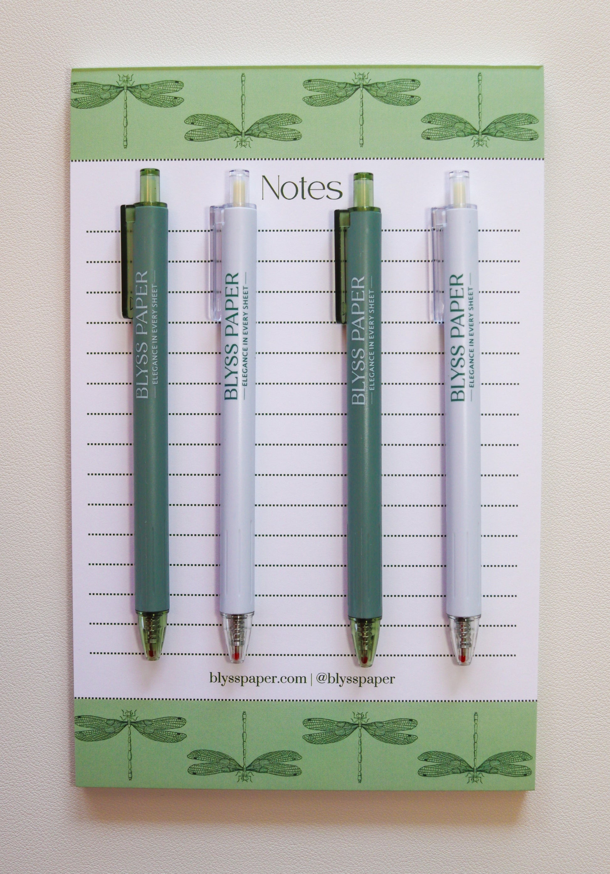 Up close view of 4 gel pens laid on top of a dragonfly notepad